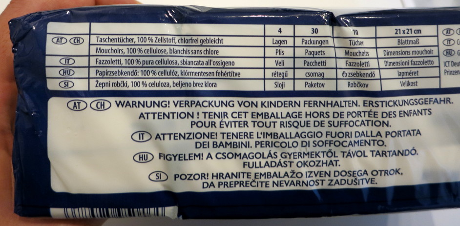 Kleingedrucktes: »Taschentücher, 100% Zellstoff, chlorfrei gebleicht« und zusätzliche Details in fünf verschiedenen Sprachen. In Großschrift und generell größeren Buchstaben auch angeschrieben: »Warnung! Verpackung von Kindern fernhalten. Erstickungsgefahr.«