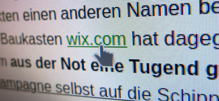 Nahaufnahme von Text auf Monitor. Ein Link mit der Bezeichnung »wix.com« steht im Zentrum und der Mauszeiger in Form einer Hand ruht darüber.