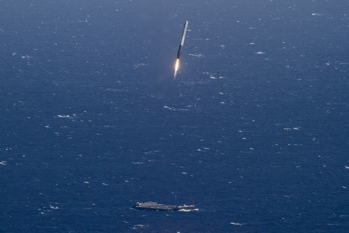 Raketenstufe mit feuerndem Triebwerk über Landeplattform im Ozean.