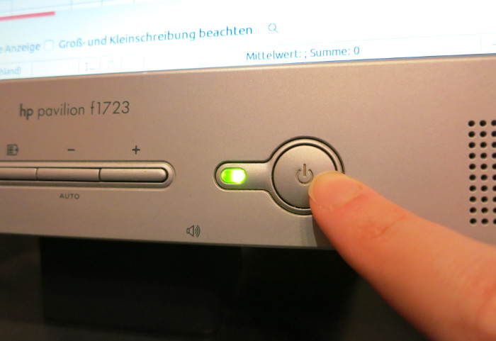 Finger drückt einen großen Einschaltknopf an einem Monitor.