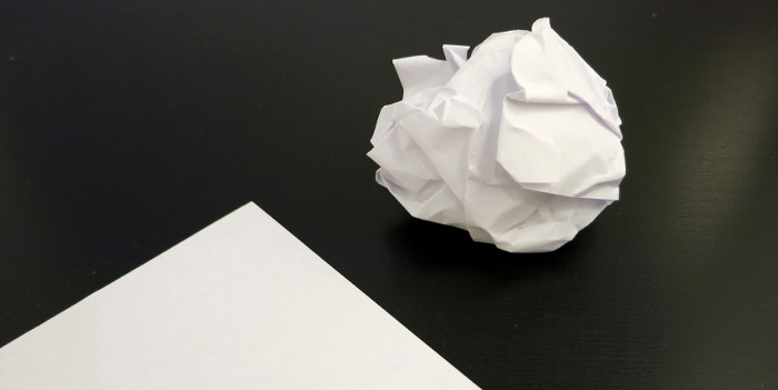 Zerknülltes Blatt Papier neben einem unzerknüllten Blatt.